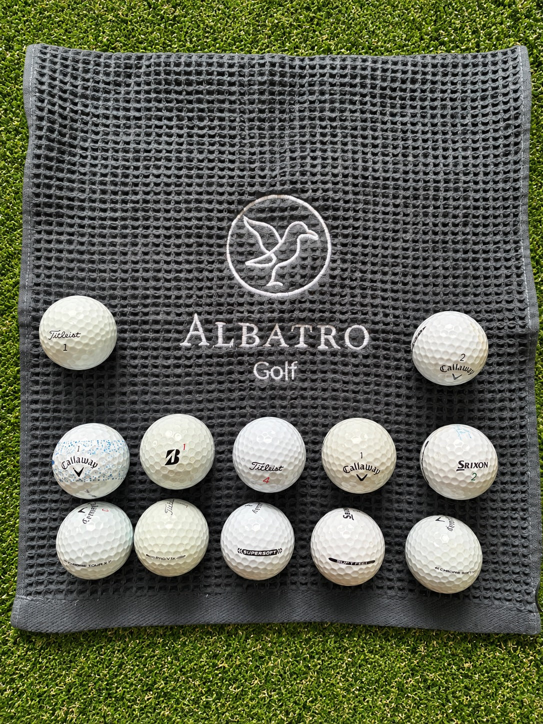 12 pelotas de golf usadas grado AAA Titleist, Callaway, Bridgestone y Srixon sobre toalla Albatro Golf en pasto