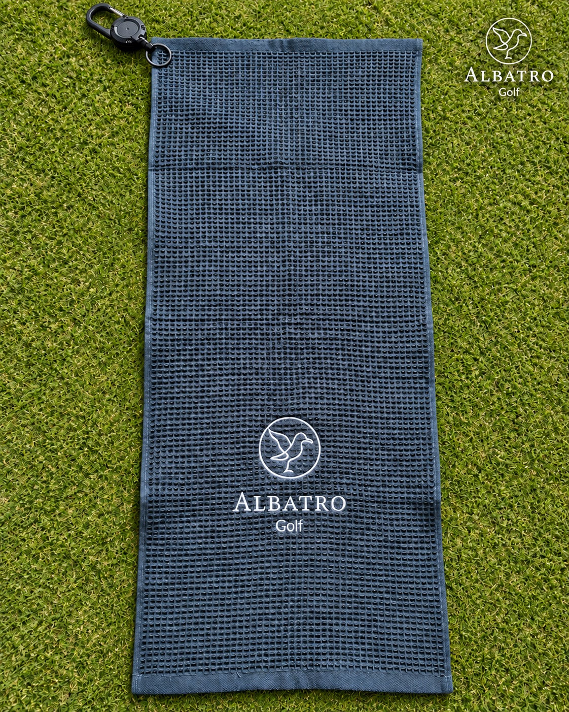 Toalla de golf Albatro extendida sobre pasto, con mosquetón y logo bordado