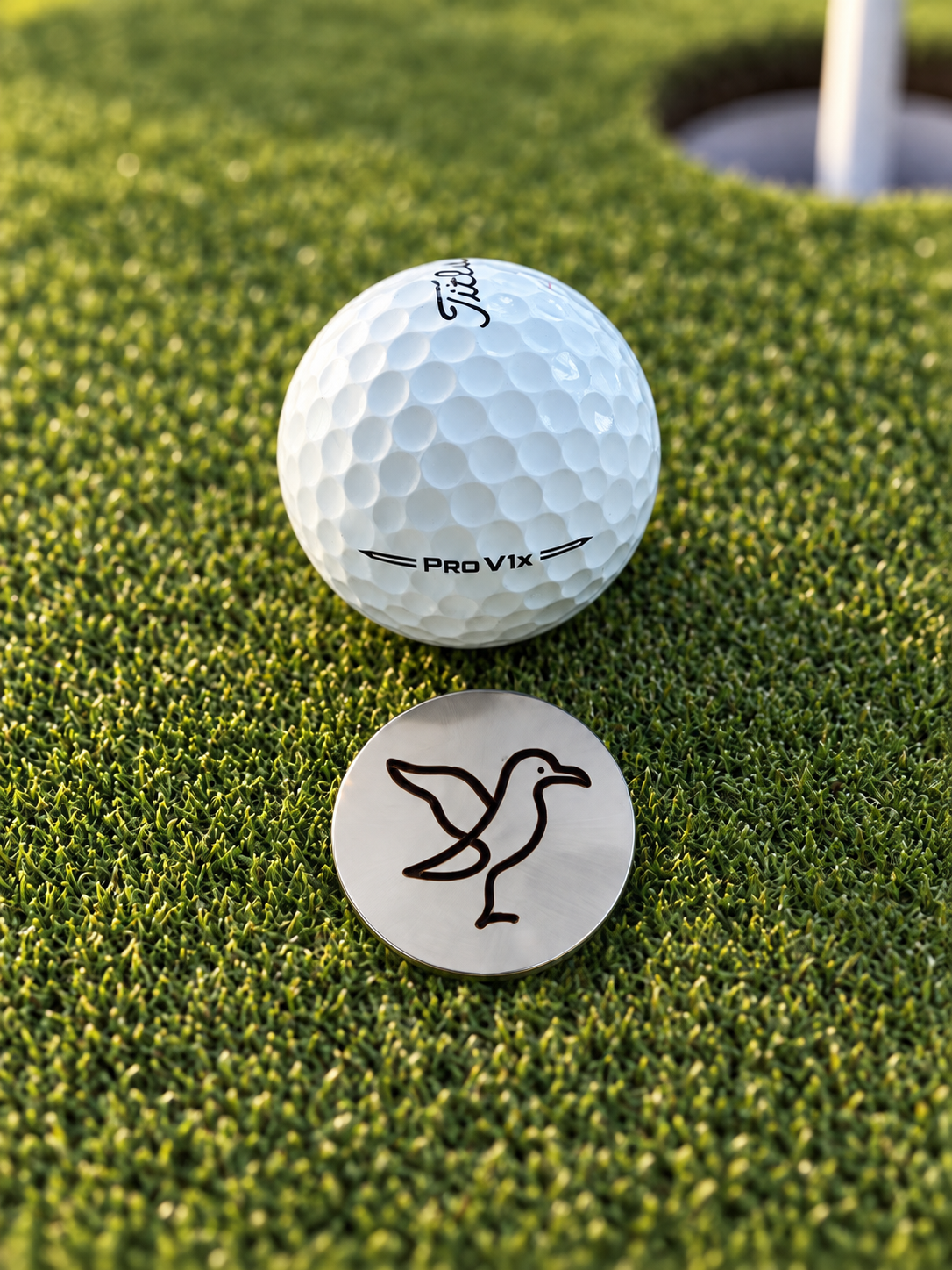 Marcador de pelota metálico Albatro junto a una pelota de golf en el green